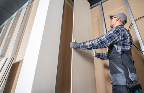 Construction worker fitting drywall piece in newly built commercial building