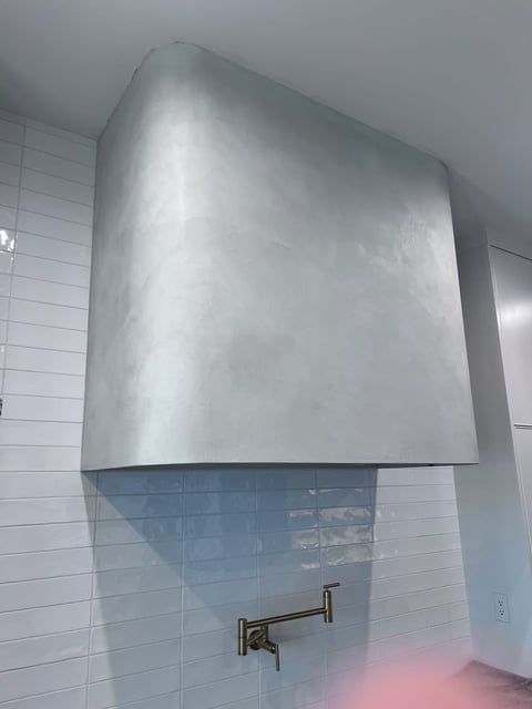Large stainless steel range hood mounted above sink with mirror and wall faucet in modern bathroom with white subway tile walls