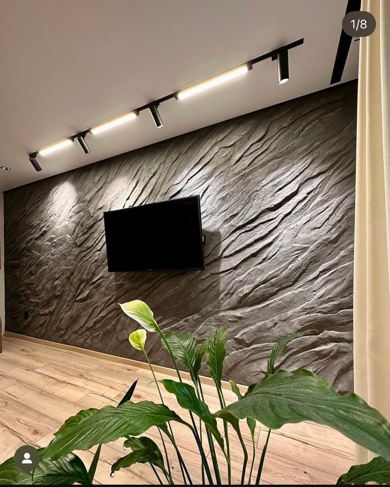 Modern living room with textured gray stone wall, wall-mounted TV, linear track lighting, wooden floor, and potted green plant