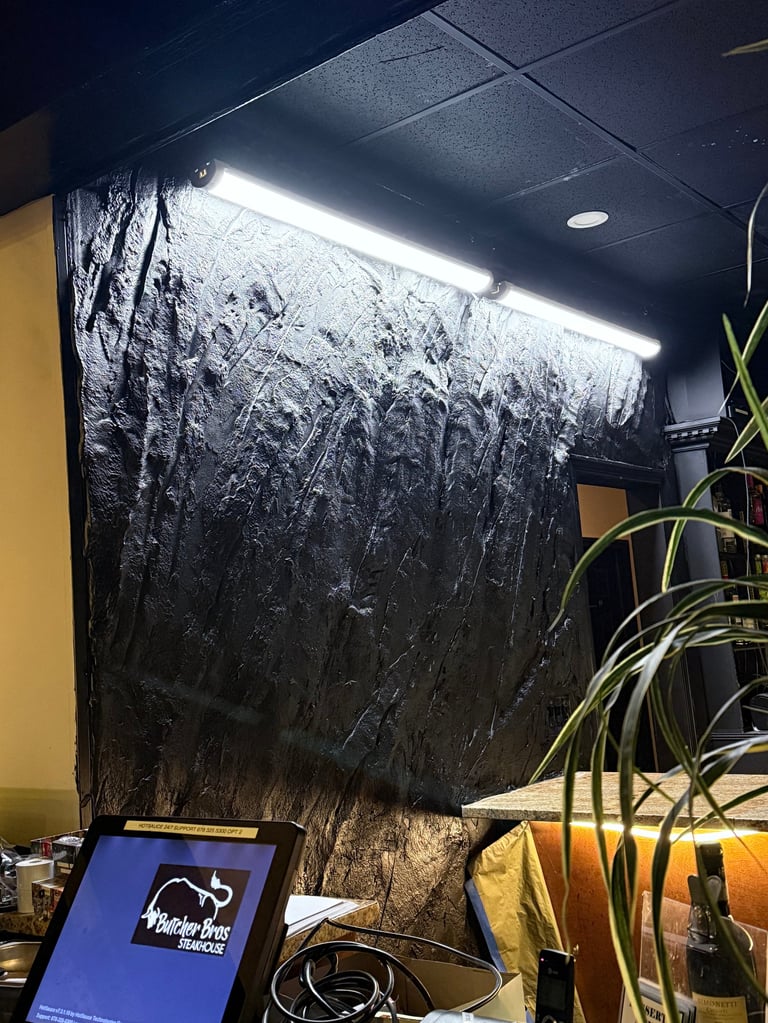 Indoor hydroponic grow setup with black reflective backdrop, LED grow lights, plant with yellow-green leaves in pot, and digital device on desk