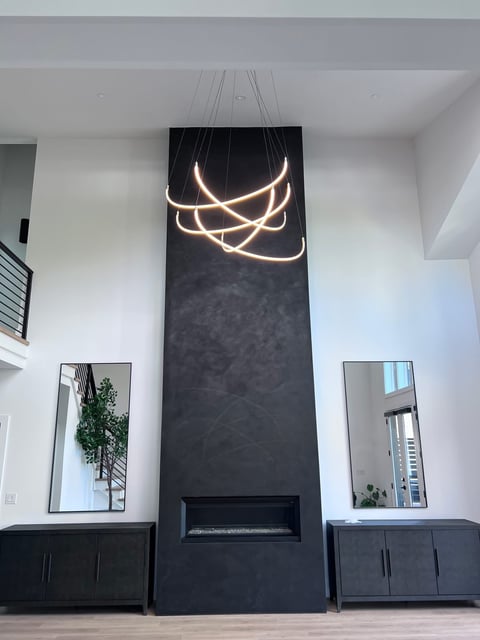 Modern living room with tall black accent wall, linear neon pendant light, fireplace, mirrored wall art, and dark cabinetry