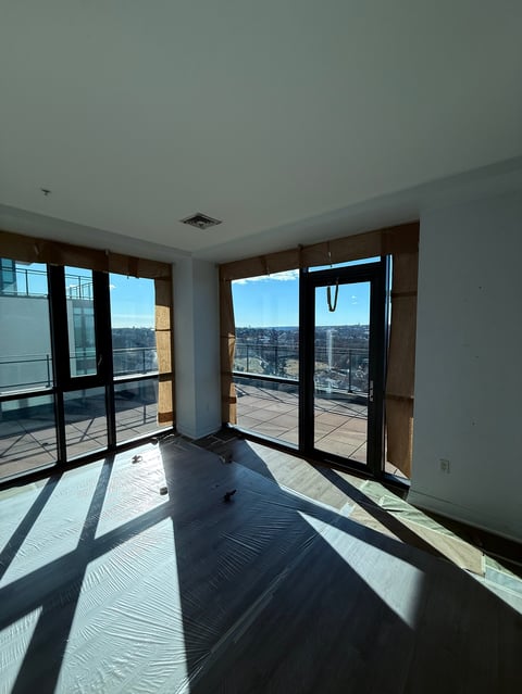 Empty modern apartment interior with floor-to-ceiling windows and glass doors opening to a balcony overlooking a city skyline
