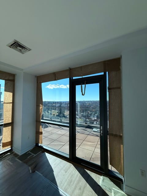 High-rise apartment interior with black-framed glass doors opening to a balcony overlooking a sprawling cityscape under blue sky