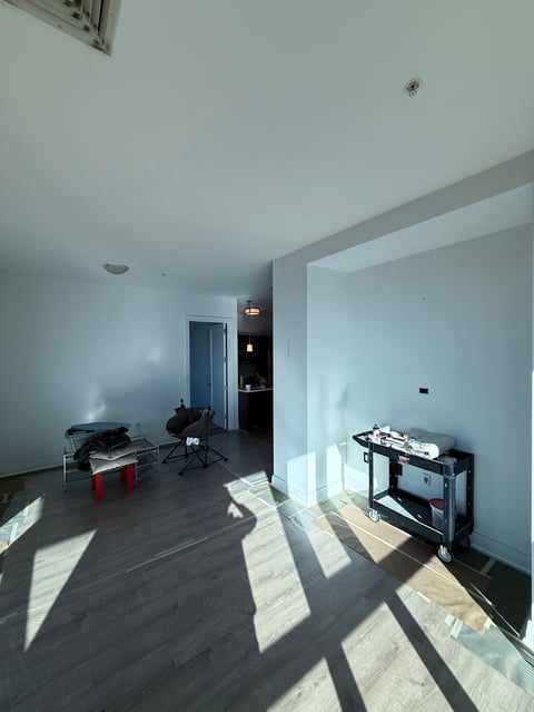 Sparse modern office or studio space with dark flooring, white walls, minimal furniture, and natural light streaming through windows