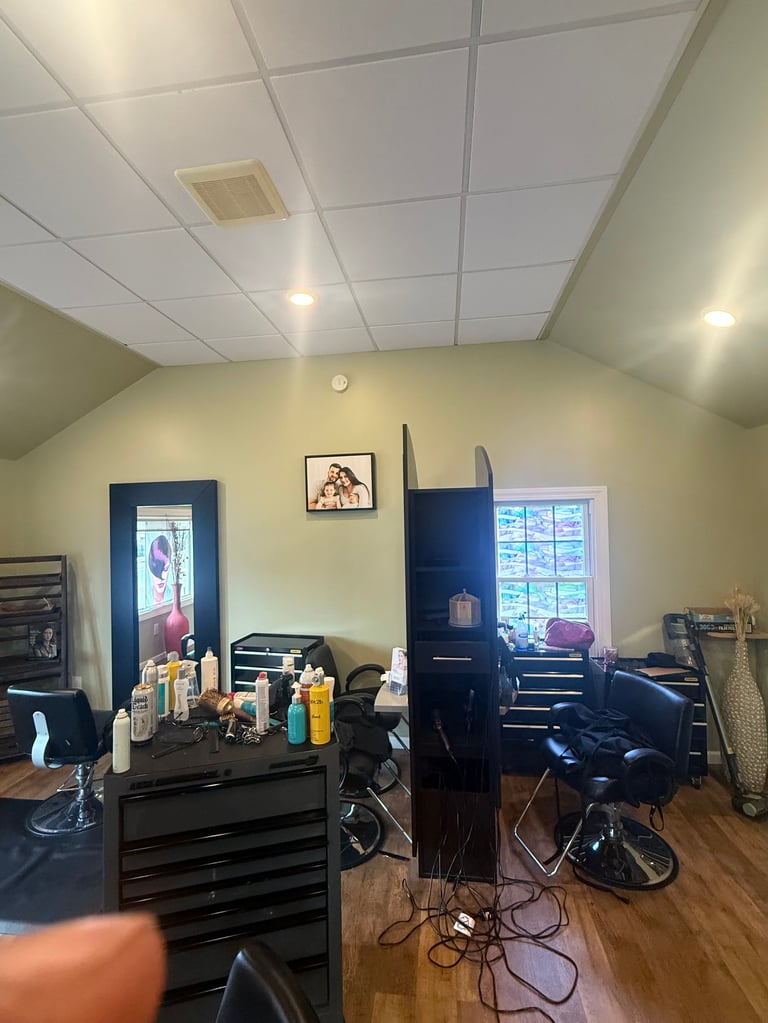 Interior of a professional hair salon with yellow walls, black styling stations, salon chairs, and product bottles on countertops