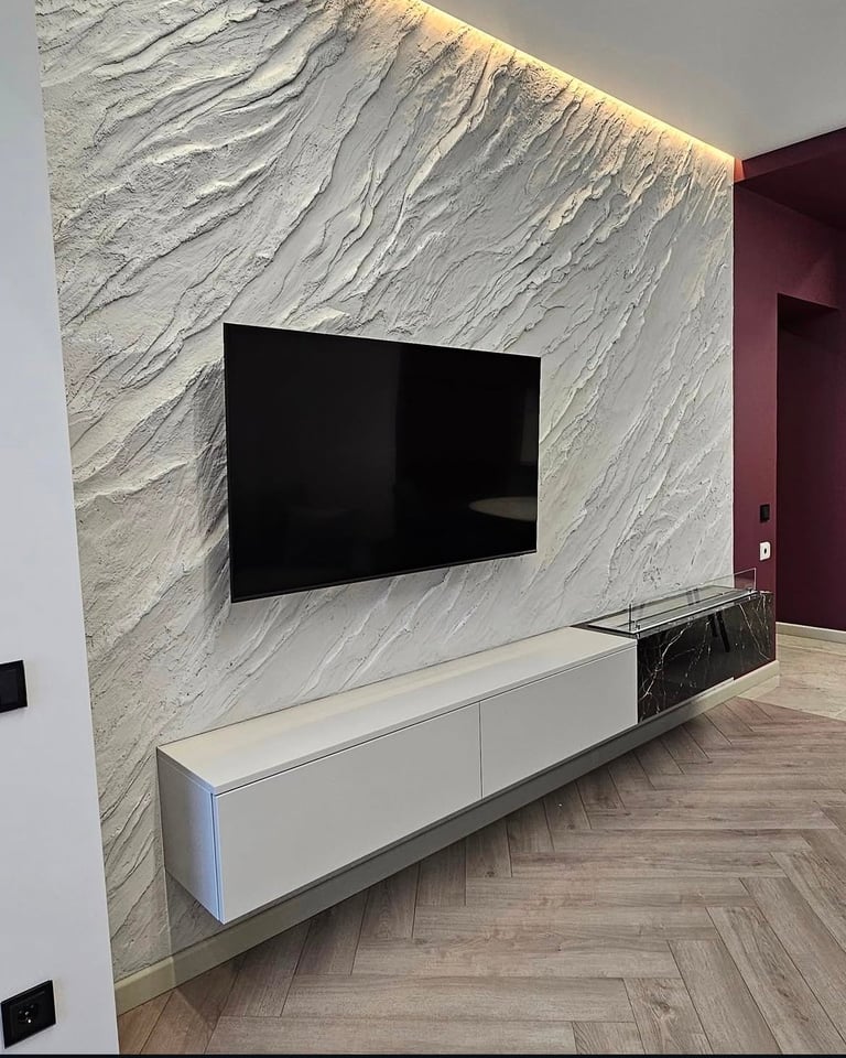 Modern living room with wall-mounted flat-screen TV on textured marble wall, white floating media console below, and burgundy accent wall