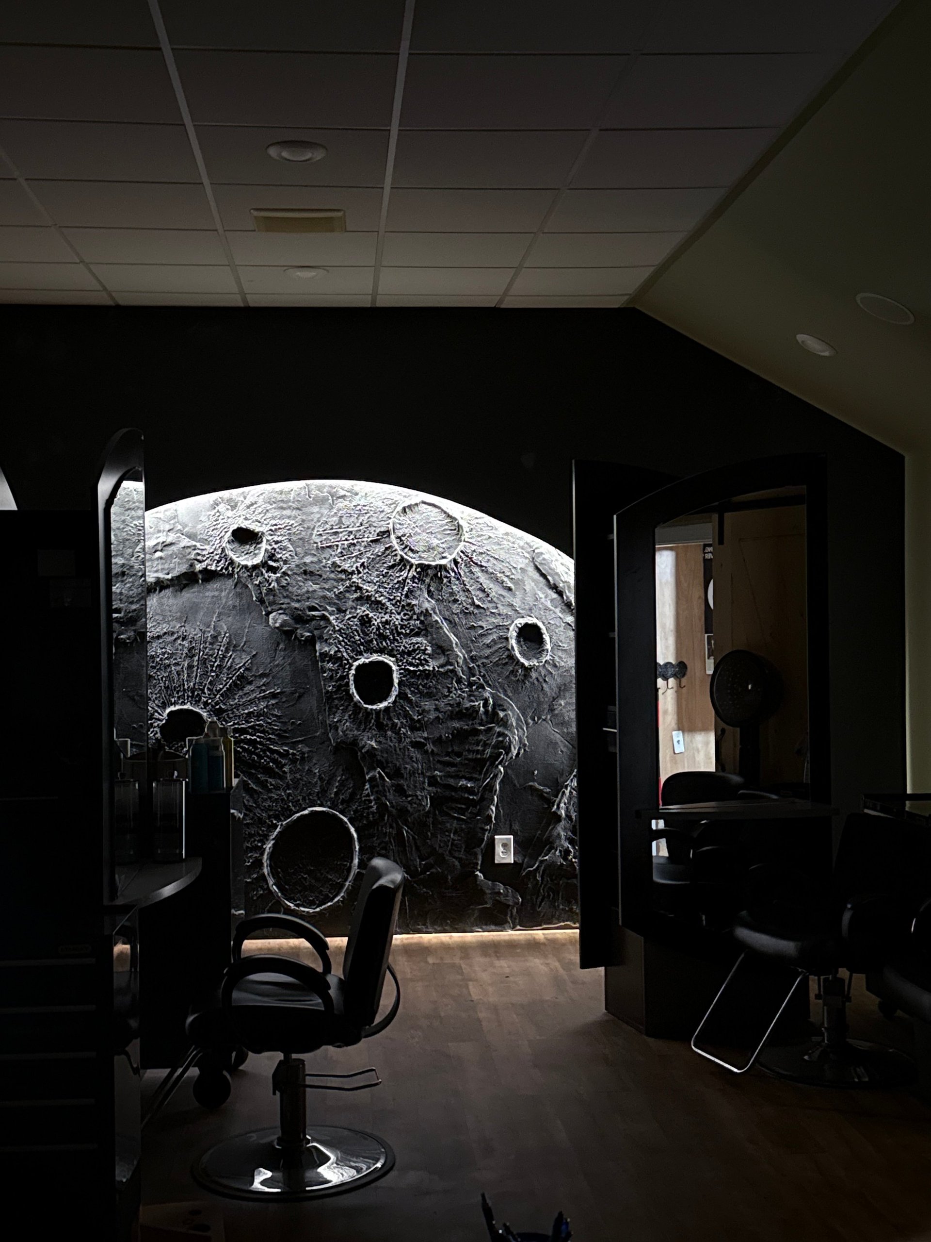 Large illuminated moon surface mural on dark wall in office space with desk chair and doorway visible