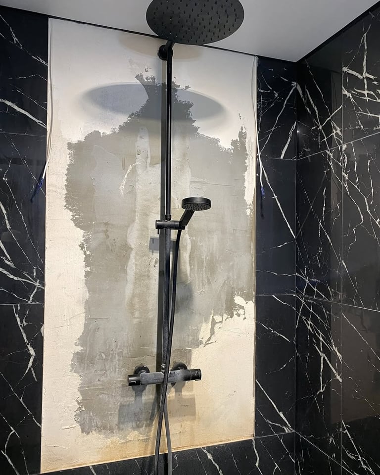 Modern black shower fixtures mounted on a cream tile wall with black marble-patterned tiles surrounding the shower enclosure