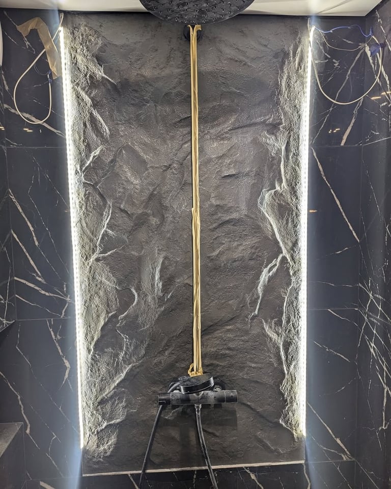 Modern bathroom shower niche with textured stone walls, gold vertical trim, and black fixtures with LED lighting