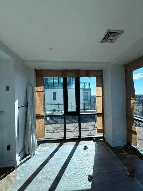 Modern apartment interior with black-framed glass doors opening to a terrace, light-filled space with white walls and light wood flooring