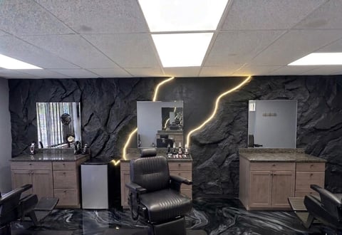 Modern salon interior with black marble walls, vanity stations, central black leather chair, and gold neon lighting accents